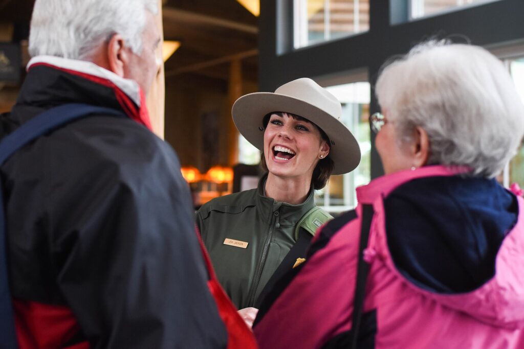 A National Park Service ranger speaking with two park visitors outdoors.